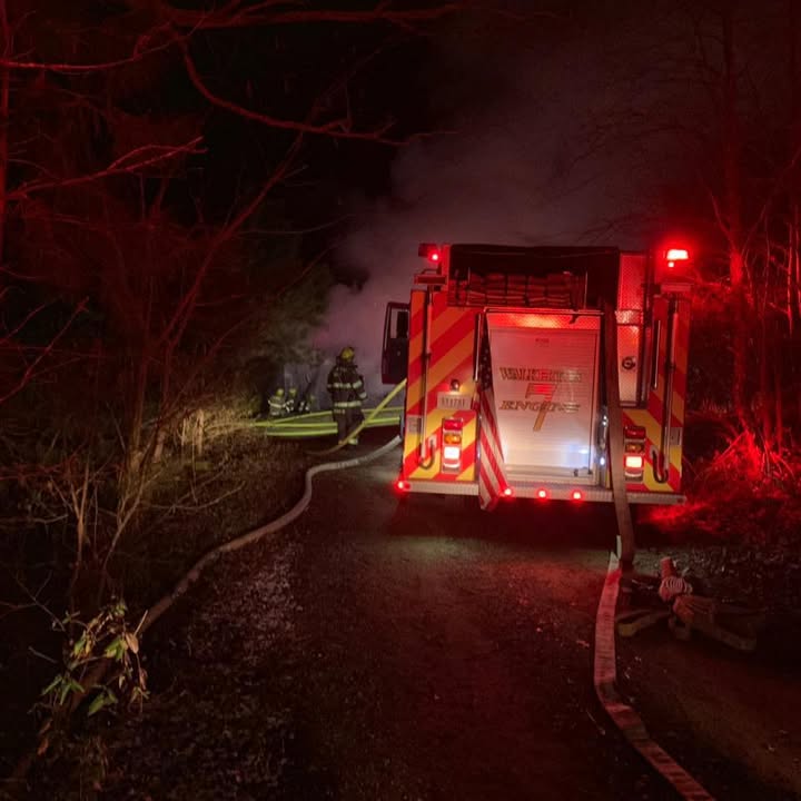 Walkerton Engine 7 crew working a hose line at a nighttime structure fire on a wooded road.